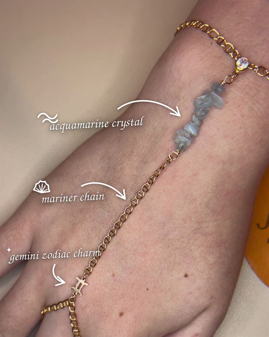 A gold mariner hand chain with aquamarine crystal and a Gemini zodiac charm.